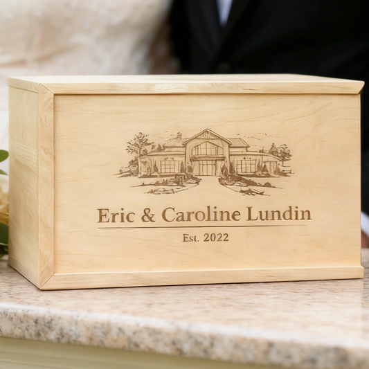 Personalized wooden box with engraved design and text, accompanied by a glass of champagne and flowers on a table.